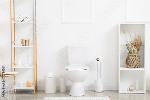 Interior of light restroom with toilet bowl  paper holder and shelf units