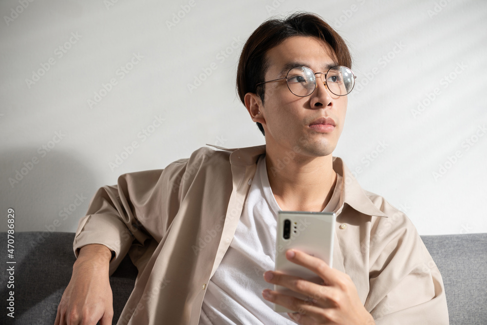 A young handsome Asian man looks confused on a cellphone, he is texting, chatting, or social media videos with friends. An Online technology, online shopping concept idea. Over white background A young handsome Asian man looks confused on a cellphone, he is texting, chatting, or social media videos with friends. An Online technology, online shopping concept idea. Over white background