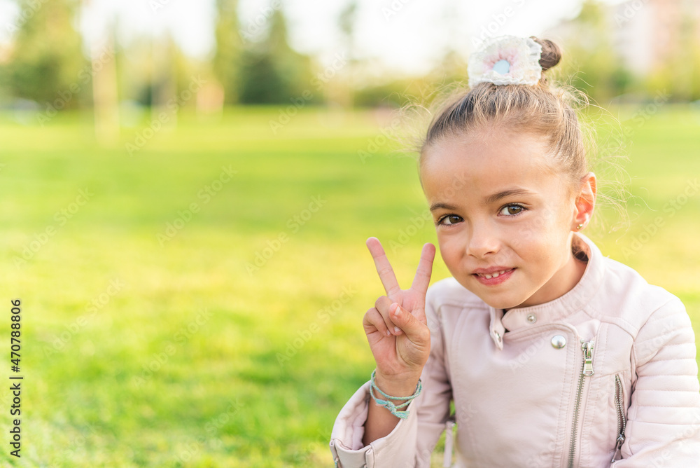 little girl sitting on grass showing peace or victory sign little girl sitting on grass showing peace or victory sign