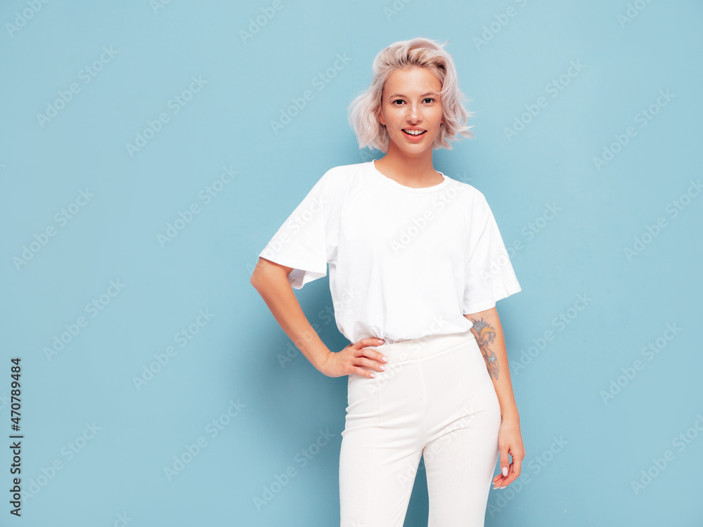 Portrait of young beautiful smiling female in trendy summer clothes. Sexy carefree woman posing near blue wall in studio. Positive blond model having fun and going crazy. Cheerful and happy Portrait of young beautiful smiling female in trendy summer clothes. Sexy carefree woman posing near blue wall in studio. Positive blond model having fun and going crazy. Cheerful and happy