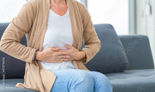Unhappy woman stomach ache, mature woman with stomach pain feeling unwell sitting in living room
