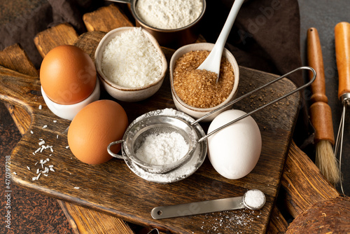 Ingredients for coconut cookies or sweet pastries on a culinary background. Eggs, coconut chips, flour, sugar and salt on a dark table