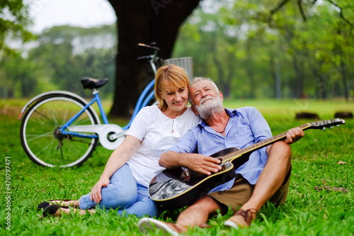 happy two caucasian elderly in park and playing guitar