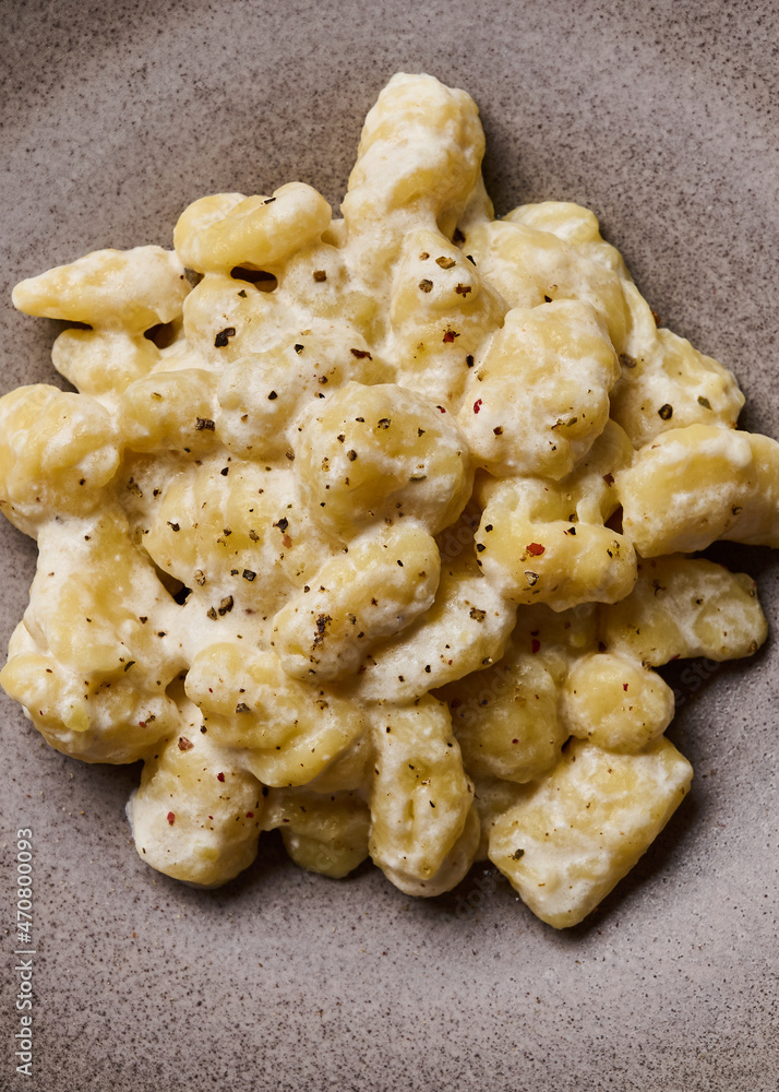 Macro vertical view potato gnocchi, prepared with potato and whole grain flour dough with cream sauce and pepper, selective focus Macro vertical view potato gnocchi, prepared with potato and whole grain flour dough with cream sauce and pepper, selective focus