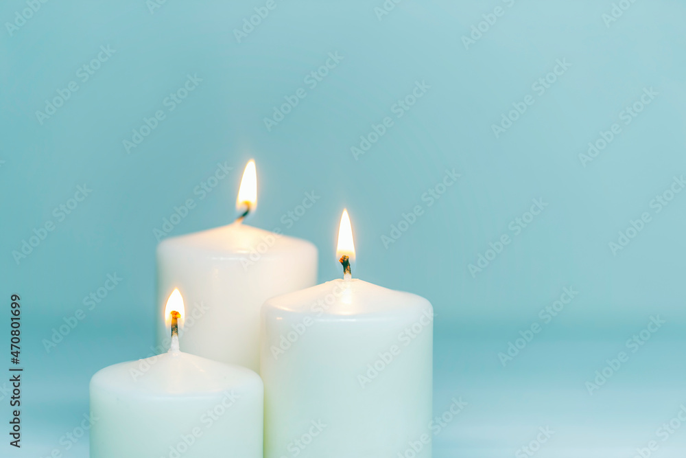 Three white candles burning on white gradient background. Front view. Horizontal composition. Set of white candles over blue background with copy space