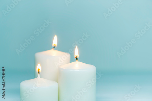 Three white candles burning on white gradient background. Front view. Horizontal composition. Set of white candles over blue background with copy space