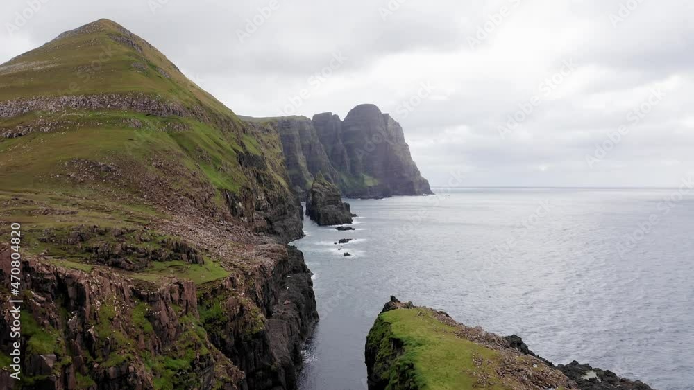 Aerial back view of huge cliffs in faroe islands, green rocky mountain,powerful ocean waves,in a cloudy summer day,green meadow and rock in wild nature,wild no house. Aerial back view of huge cliffs in faroe islands, green rocky mountain,powerful ocean waves,in a cloudy summer day,green meadow and rock in wild nature,wild no house.