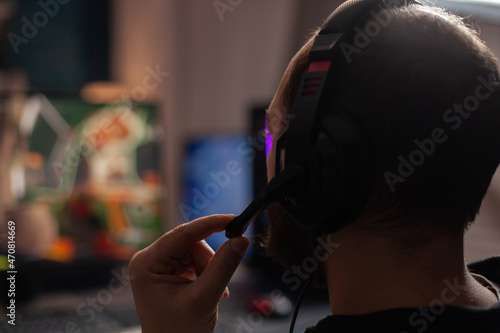 Close up of person streaming using microphone on headphones with computer. Man live streaming video games play on monitor, talking to audience and playing online games for social media.
