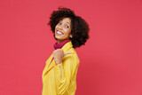Charming bright happy swanky young curly black latin woman 20s years old wears yellow jacket pointing finger back on workspace area copy space mock up isolated on plain red background studio portrait.