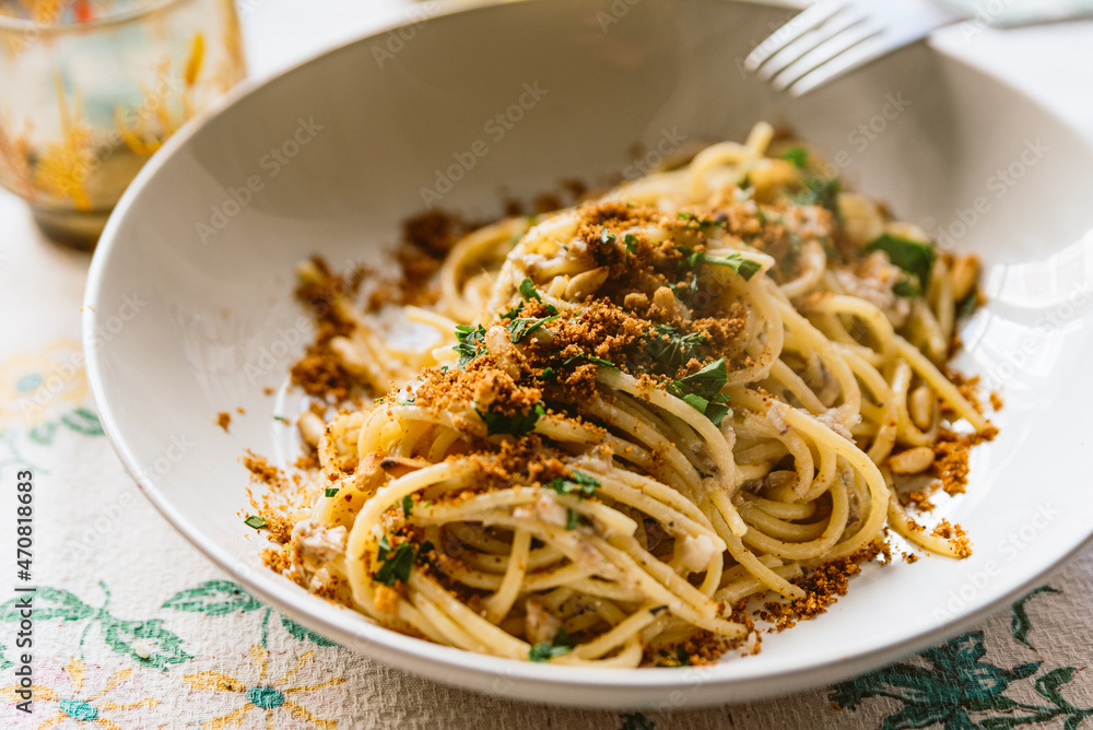 homemade italian pasta dish known as "pasta con le sarde" on table cloth, made with spaghetti, sardines, parsley, pine nuts and breadcrumbs. Classic italian regional cuisine. - obrazy, fototapety, plakaty 