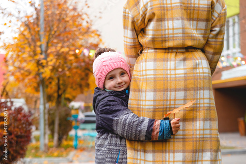 Little girl hugs her mom on a walk along the autumn street. Fall colors