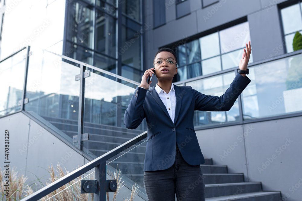 Angry and serious businesswoman talking on the phone outside the office, African American woman dressed in business clothes, communicating with colleagues Angry and serious businesswoman talking on the phone outside the office, African American woman dressed in business clothes, communicating with colleagues