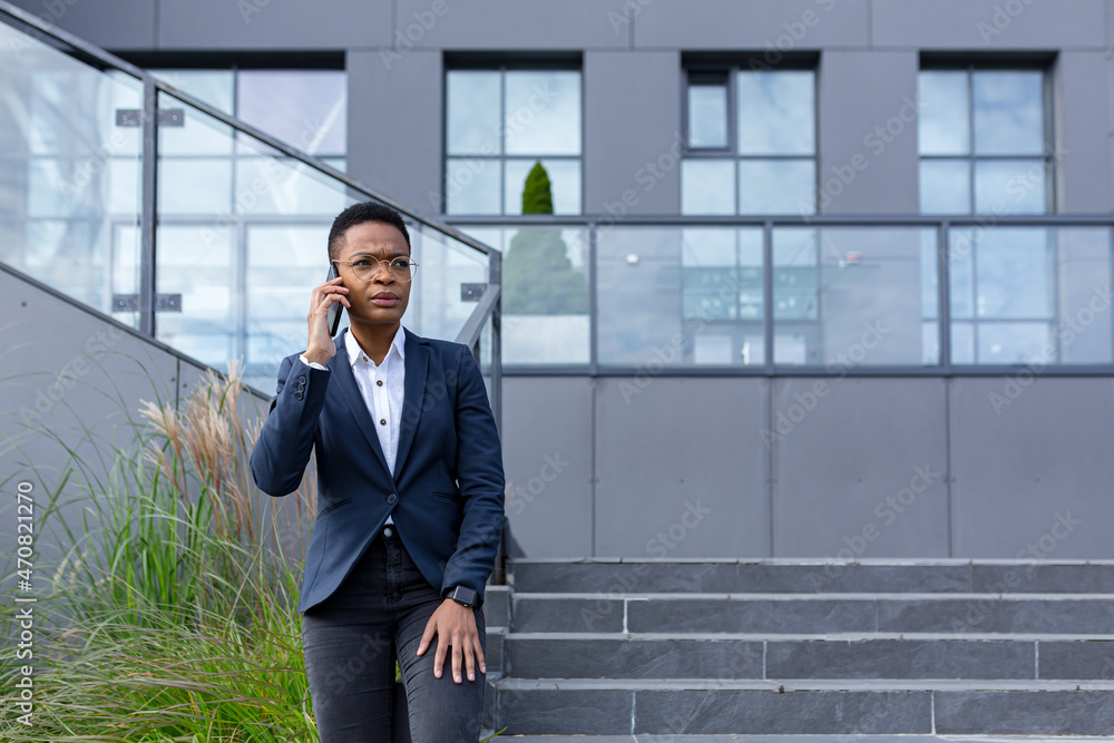 Angry and serious businesswoman talking on the phone outside the office, African American woman dressed in business clothes, communicating with colleagues Angry and serious businesswoman talking on the phone outside the office, African American woman dressed in business clothes, communicating with colleagues