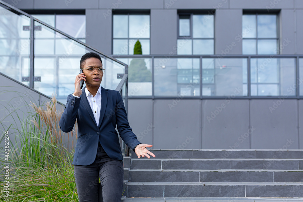 Angry and serious businesswoman talking on the phone outside the office, African American woman dressed in business clothes, communicating with colleagues Angry and serious businesswoman talking on the phone outside the office, African American woman dressed in business clothes, communicating with colleagues