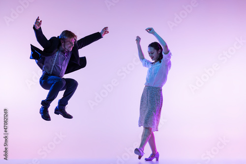 Couple of dancers, young man and woman in vintage retro style outfits dancing swing dance isolated on lilac color background in neon light