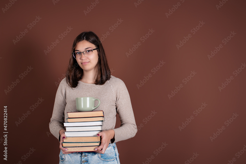 A beautiful and smart girl student is holding books in her hands, preparing for the exam. A woman stands on a brown background. A beautiful and smart girl student is holding books in her hands, preparing for the exam. A woman stands on a brown background.