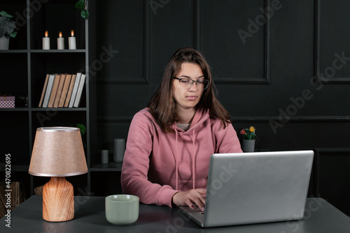 Pretty woman is typing on the laptop keyboard while sitting in the office. A student is preparing for an online conference.