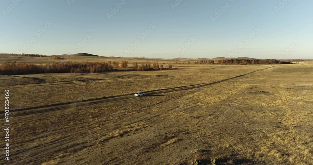 One white crossover SUV car driving alone road trip, travel on gravel road through dense colorful forest corridor at autumn sunny sunset - Aerial drone wide view One white crossover SUV car driving alone road trip, travel on gravel road through dense colorful forest corridor at autumn sunny sunset - Aerial drone wide view