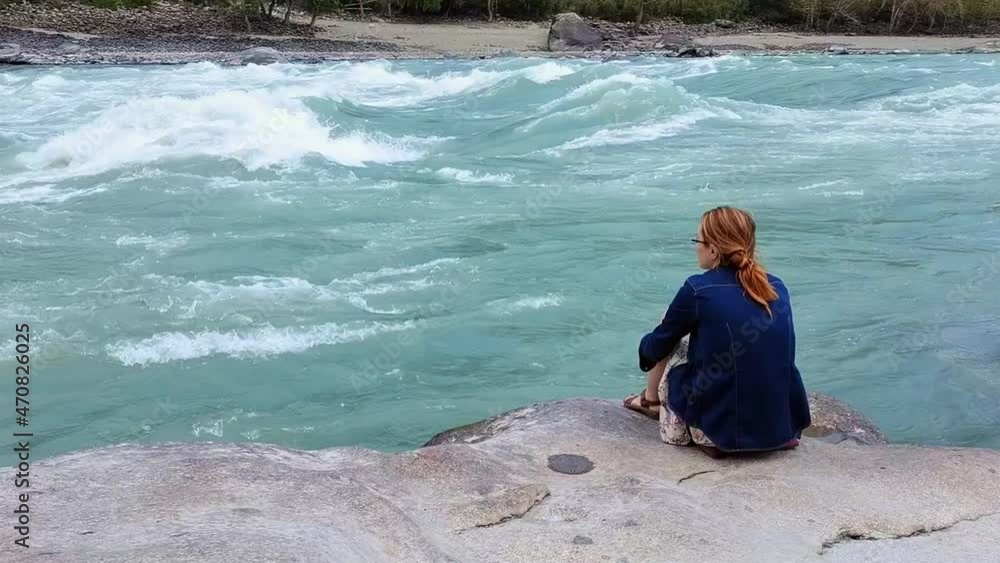 Young woman sitting on a stone, enjoying magnificent beauty of mountain river, view from the back. Nature female lover rests in scenery place. Young woman sitting on a stone, enjoying magnificent beauty of mountain river, view from the back. Nature female lover rests in scenery place.