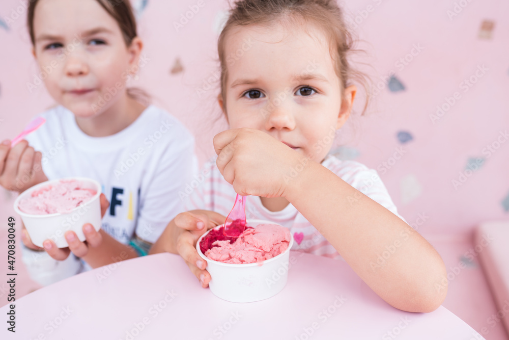 Summer food. Two adorable caucasian girls eating ice cream in cafe. Happy sisters are having sweets in gelateria. Childhood concept. Selective focus Summer food. Two adorable caucasian girls eating ice cream in cafe. Happy sisters are having sweets in gelateria. Childhood concept. Selective focus