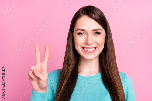 Photo portrait of girl showing peace v-sign smiling in casual outfit isolated on pastel pink color background