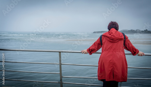 Rear view of a reflective woman red trench coat contemplating the sea on a beach on a summer vacation, outdoors. Middle-aged travel lifestyle. photo