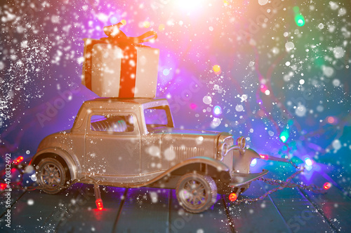 Retro car with a gift on the roof against the background of Christmas lights. © Elena Blokhina
