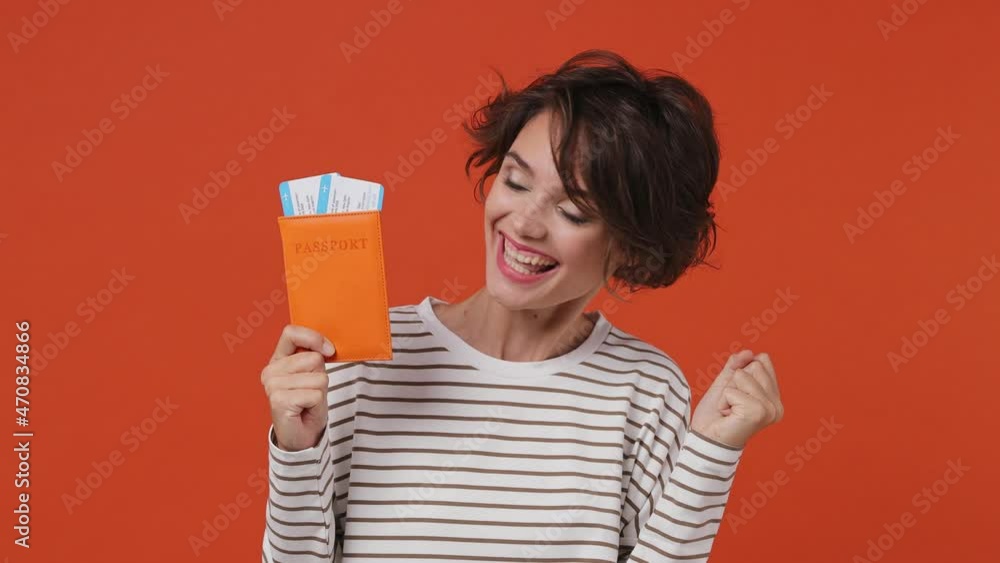 Traveler tourist young brunette woman 20s years old wears striped shirt hold passport boarding pass tickets passenger traveling abroad on weekends isolated on plain orange background studio portrait Traveler tourist young brunette woman 20s years old wears striped shirt hold passport boarding pass tickets passenger traveling abroad on weekends isolated on plain orange background studio portrait