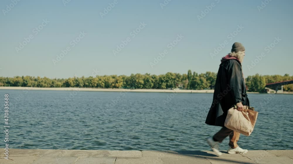 Elderly beggar walking along the river in park, need of housing, unemployment Elderly beggar walking along the river in park, need of housing, unemployment