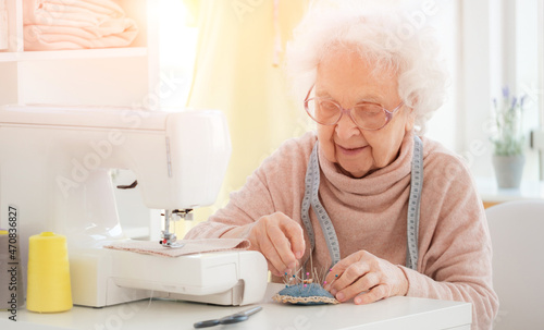 Lovely aged woman sewing at workshop