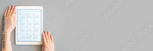 tablet computer with an open app of calendar for unspecified unknown date year without date in womans hands on gray background. business or to do list goals. top view, flat lay. banner. space for text