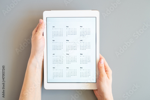 tablet computer with an open app of calendar for unspecified unknown date year without date in a womans hands on a gray background. concept business or to do list goals. top view, flat lay
