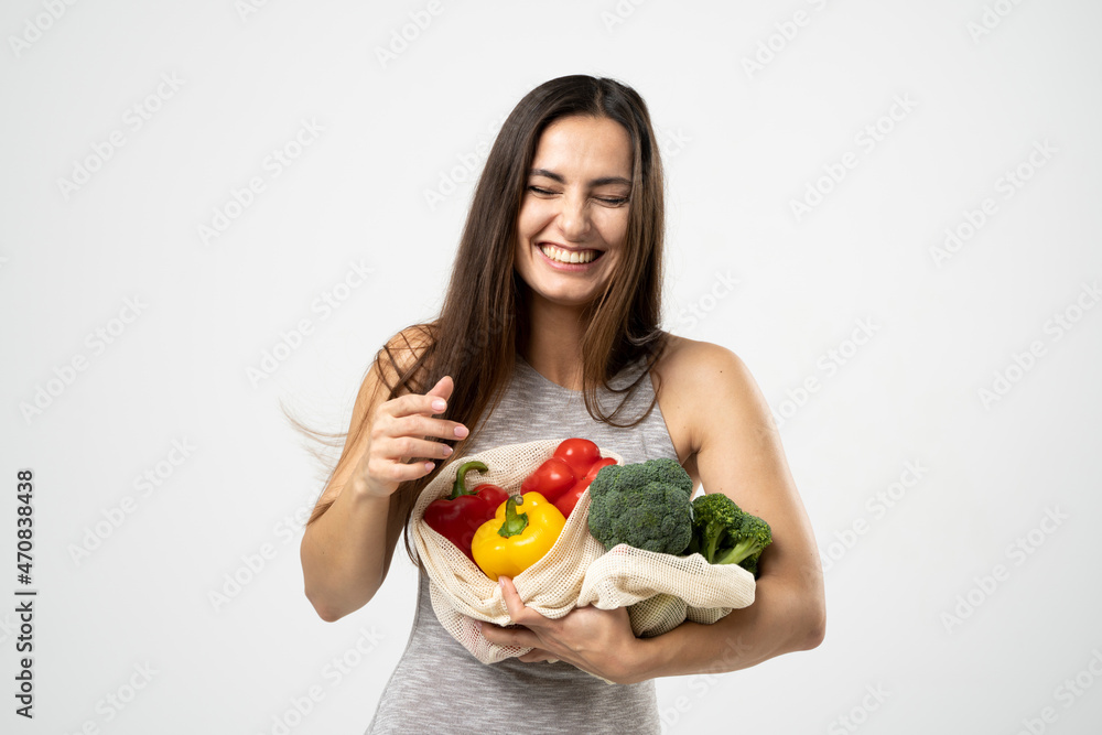 Smiling brunette girl is holding mesh shopping bag with vegetables, greens without plastic bags. Zero waste, plastic free Eco friendly concept. Sustainable lifestyle. Smiling brunette girl is holding mesh shopping bag with vegetables, greens without plastic bags. Zero waste, plastic free Eco friendly concept. Sustainable lifestyle.