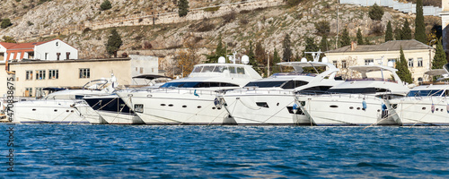 Scenic view of many luxury sailing fishing boat and charter rental speedboats moored at mountain harbor lake bay against mountain landscape backgound on sunny day. Sea marina vessel pier sorage dock photo