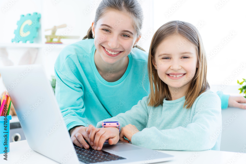 Smiling sisters next to modern laptop in light room Smiling sisters next to modern laptop in light room