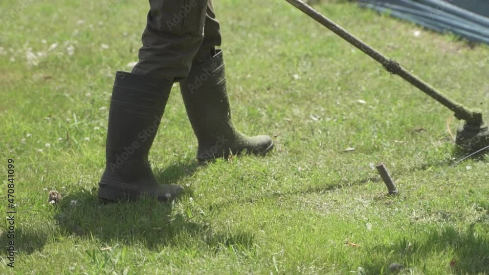 Close up slow motion of person in garden cutting lawn with brushcutter during sunlight Close up slow motion of person in garden cutting lawn with brushcutter during sunlight