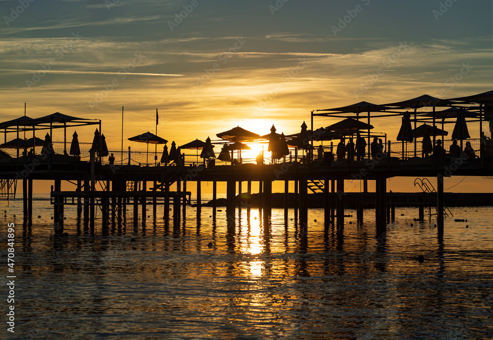 pier with umbrellas and sunbeds. silhouettes. beautiful sunset on sea. 