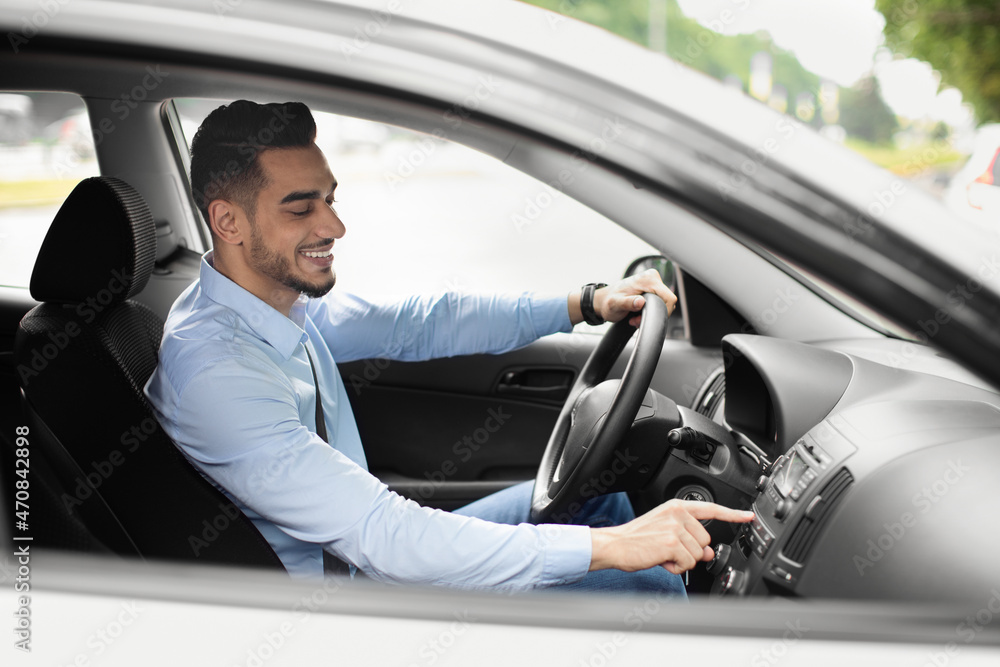 Happy middle eastern businessman turning on music before driving