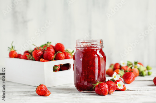 Homemade strawberry preserves or jam in a mason jar surrounded by fresh organic strawberries. Selective focus with blurred foreground and background. photo