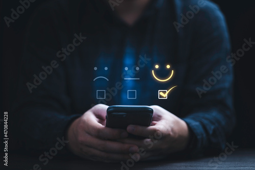 Businessman using smartphone for select smiley face icon for client evaluation and customer satisfaction after use product and service concept.