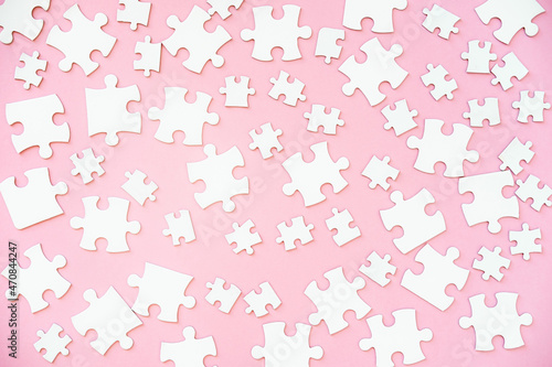 White puzzle pieces of different size scattered over pink background, top view photo