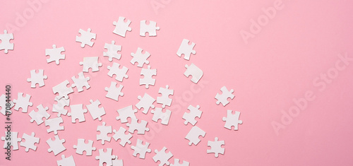 Scattering of white jigsaw puzzle pieces on pink background with copy space, top view photo