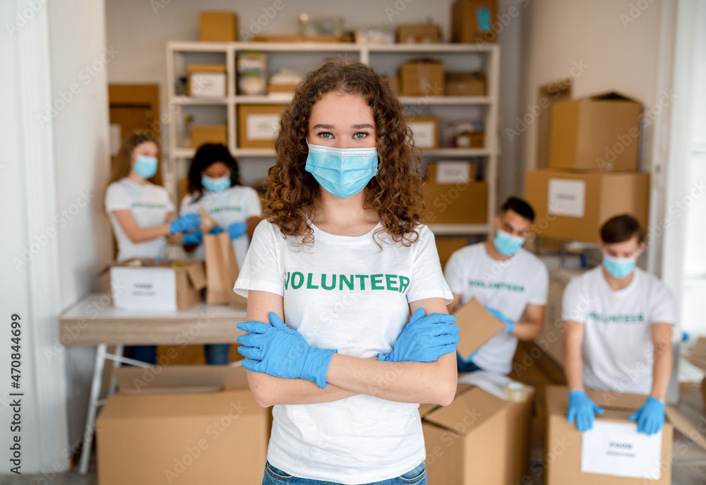 Charity center. Young female volunteer in medical mask posing with crossed hands, working in volunteering organization