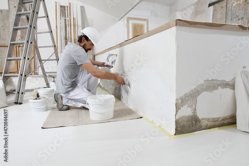 plasterer man at work, take the mortar from the bucket with trowel to plastering the wall of interior construction house site and wear helmet,