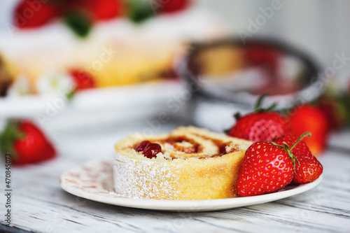 Homemade strawberry shortcake cake roll or Roulade with a berry jam filling and powdered sugar with mint leaves. Dessert over a white rustic table. Selective focus with blurred foreground background