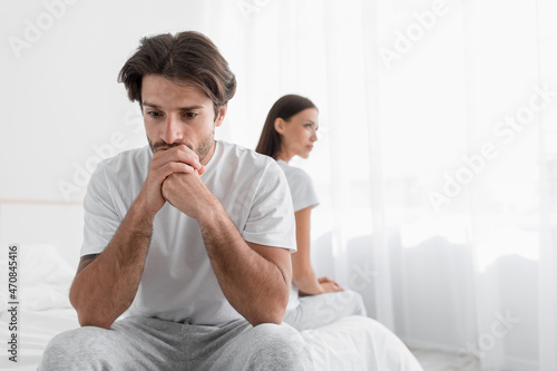 Depressed young caucasian husband with stubble sits on bed and sad, ignoring offended lady in bedroom © Prostock-studio