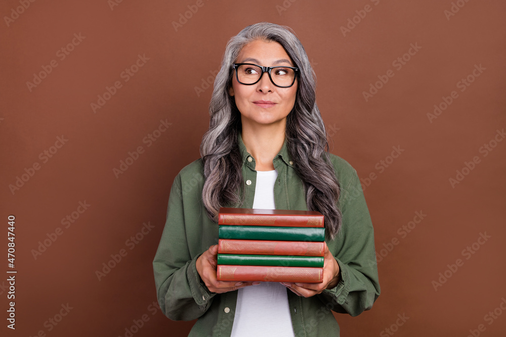 Photo of good aged white hairdo lady hold books look empty space wear khaki shirt eyewear isolated on brown color background Photo of good aged white hairdo lady hold books look empty space wear khaki shirt eyewear isolated on brown color background
