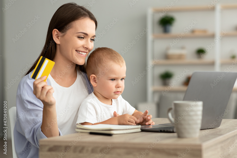 Happy Young Woman Holding Toddler Baby And Making Online Shopping At Home Happy Young Woman Holding Toddler Baby And Making Online Shopping At Home