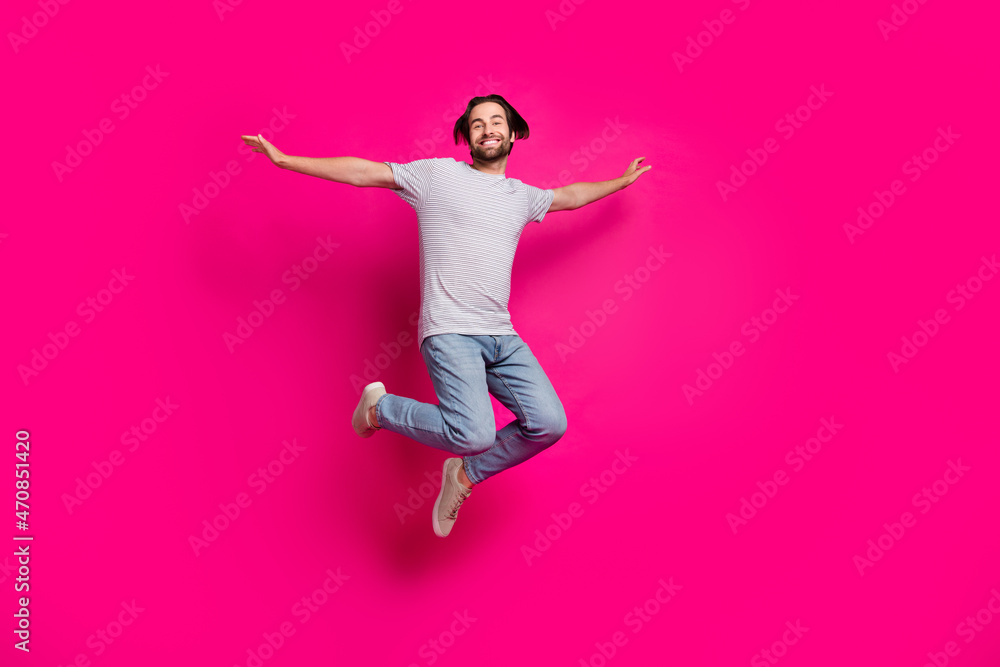 Photo of inspired tourist guy jump plane pose trip wear striped t-shirt jeans sneakers isolated pink color background