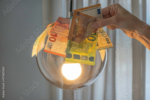 Euro bills over glowing lamp and a woman hand holding Euro banknote. Electricity cost, electricity bill payment, expensive energy concept